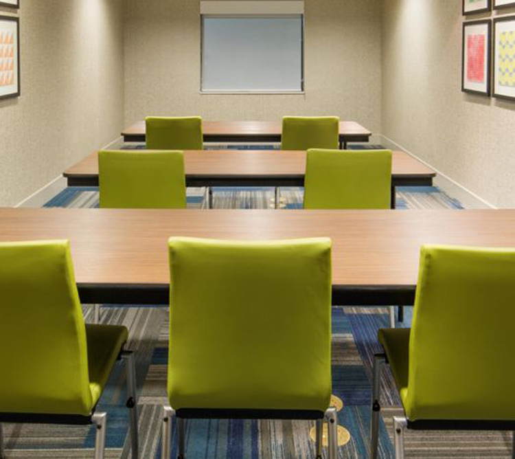 Small conference room with lime green chairs, wooden tables, and framed art on beige walls.