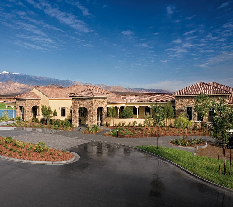 Large, single-story building with stone accents, arched entry, and landscaped grounds under a blue sky.