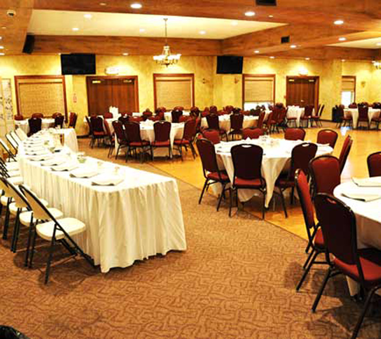 A banquet hall with round tables, red chairs, and white tablecloths set up for an event.