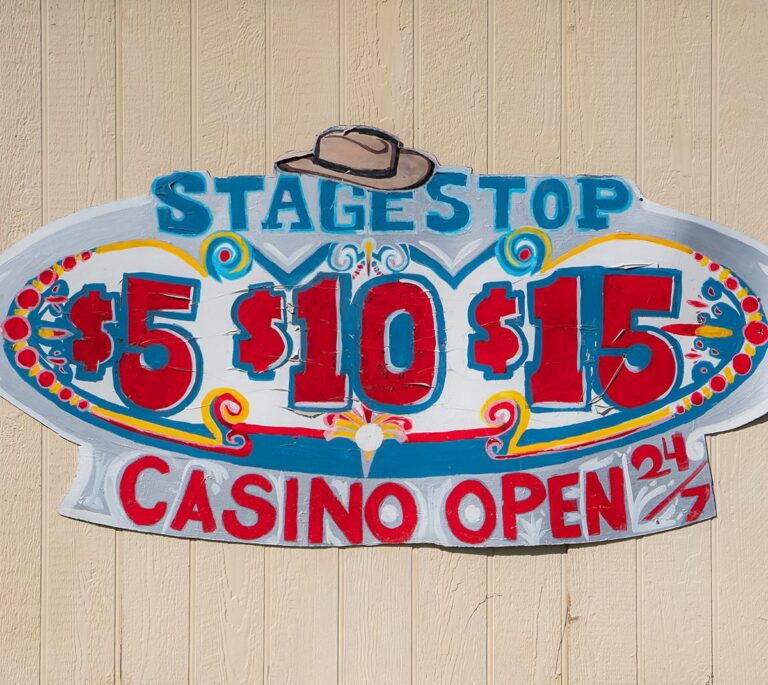 Hand-painted sign reading Stage Stop $5 $10 $15 Casino Open 24/7 with a hat illustration on top.