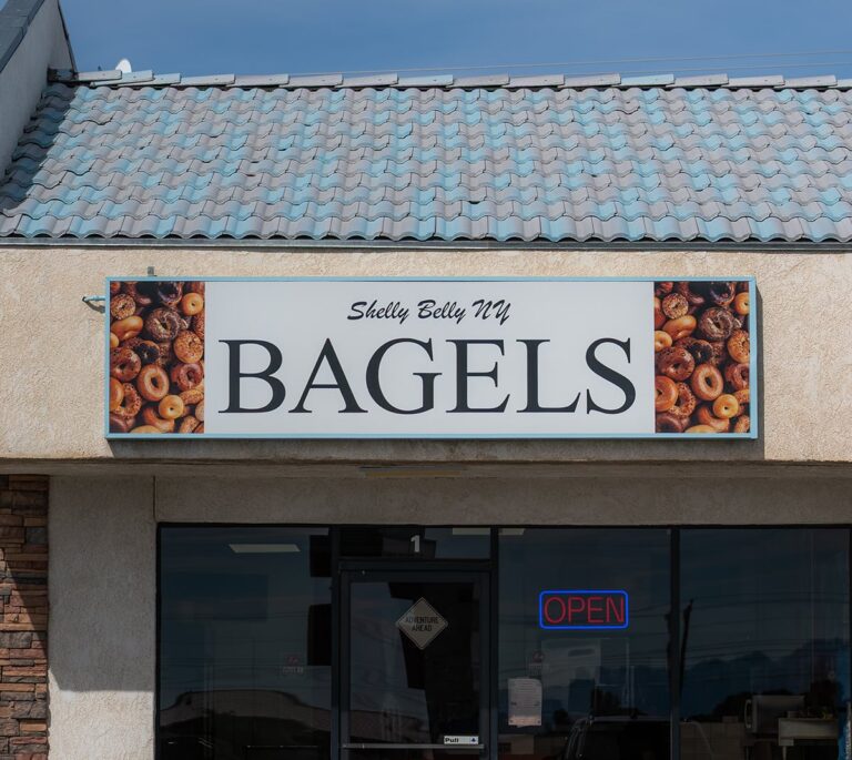 Storefront sign reads Shelly Belly NY Bagels with bagel images; OPEN sign is lit in the window.