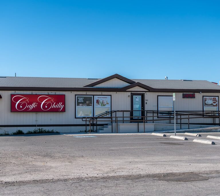 Single-story Cafe Chilly restaurant with a red sign, ramp access, and an empty parking lot under blue sky.