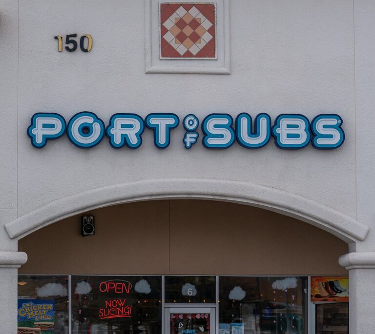 Storefront with a Port of Subs sign above a door and windows, with OPEN and menu signs visible.