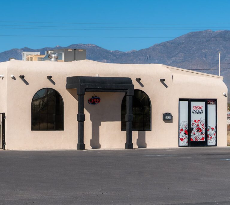 A sushi restaurant with an open sign, arched windows, and mountains in the background.