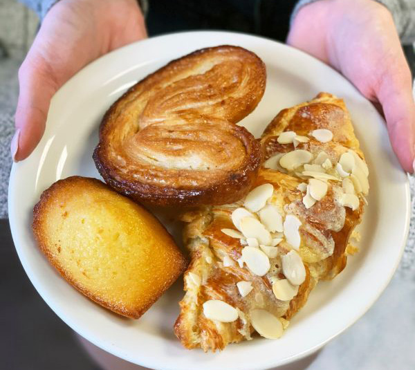 A plate with a palmier pastry, a madeleine, and an almond croissant being held in both hands.