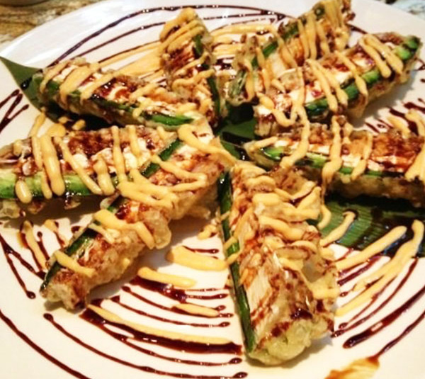 Sliced sushi rolls topped with sauce and drizzle, arranged on a white plate with decorative sauces.