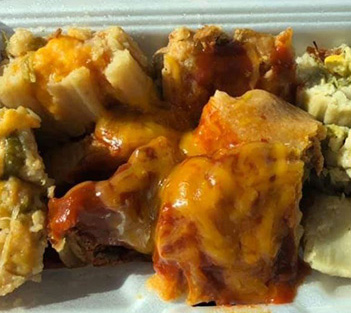 Tamales topped with melted cheddar cheese and red sauce in a white takeout container.