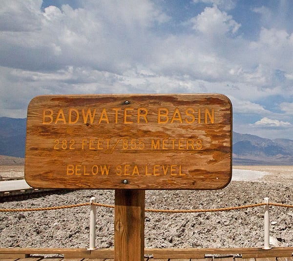 Wooden sign reading Badwater Basin 282 feet/ 855 meters below sea level with desert landscape behind.