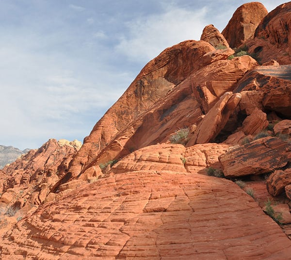 Red sandstone rock formations with striations under a partly cloudy sky.