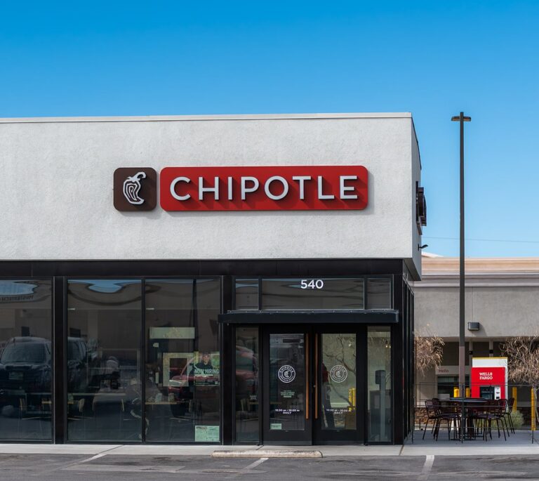 Chipotle restaurant exterior with logo and outdoor seating, under a clear blue sky.