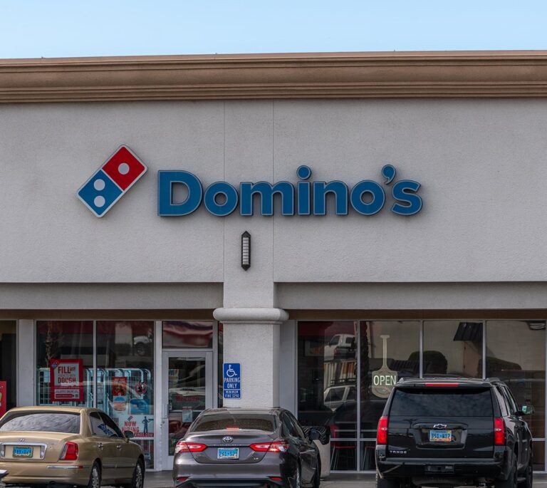 Domino’s Pizza storefront with parked cars in front and a visible handicap parking sign.