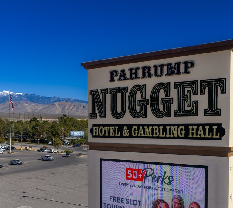 Sign for Pahrump Nugget Hotel & Gambling Hall with mountains and a parking lot in the background.