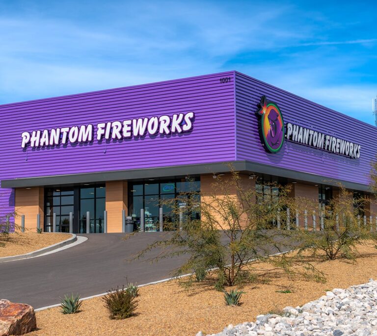 A purple Phantom Fireworks store with large logo and sign, surrounded by rocks and desert plants.