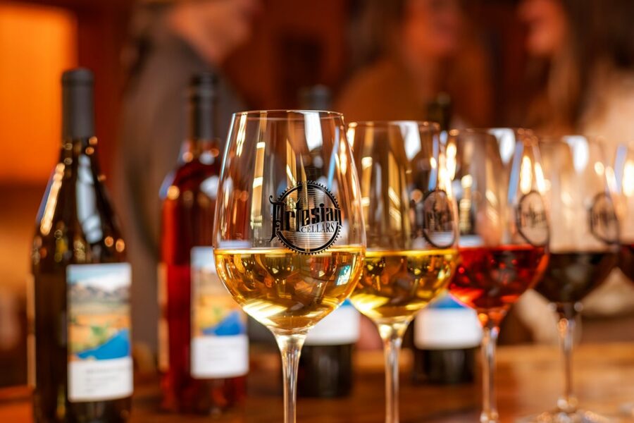 Close-up of wine glasses and bottles on a bar, with two blurred people talking in the background.