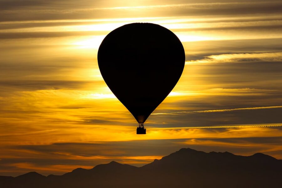 A hot air balloon silhouetted against a golden sunset sky with mountains in the background.