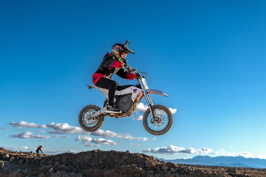A person on a dirt bike jumps over a rocky hill with a clear blue sky in the background.