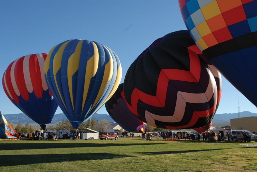 Colorful hot air balloons being prepared for launch on a grassy field with mountains in the background.
