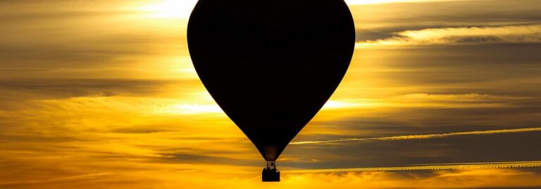 Silhouette of a hot air balloon flying against a golden sky during sunset.