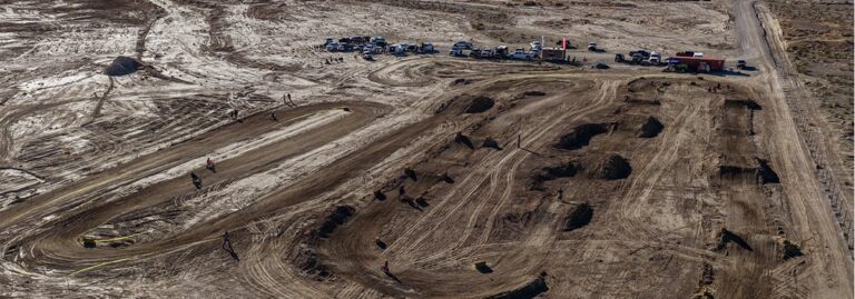 Aerial view of a dirt motocross track with vehicles and people gathered along the edge.