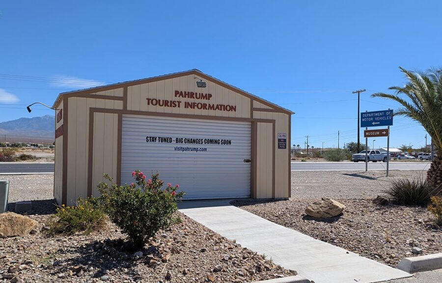 Small tan building labeled Pahrump Tourist Information with a closed garage door and desert landscaping.