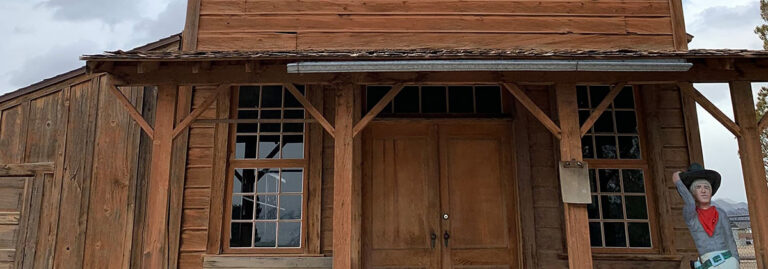 Old wooden western-style building with double doors and a cowboy cutout standing to the right.