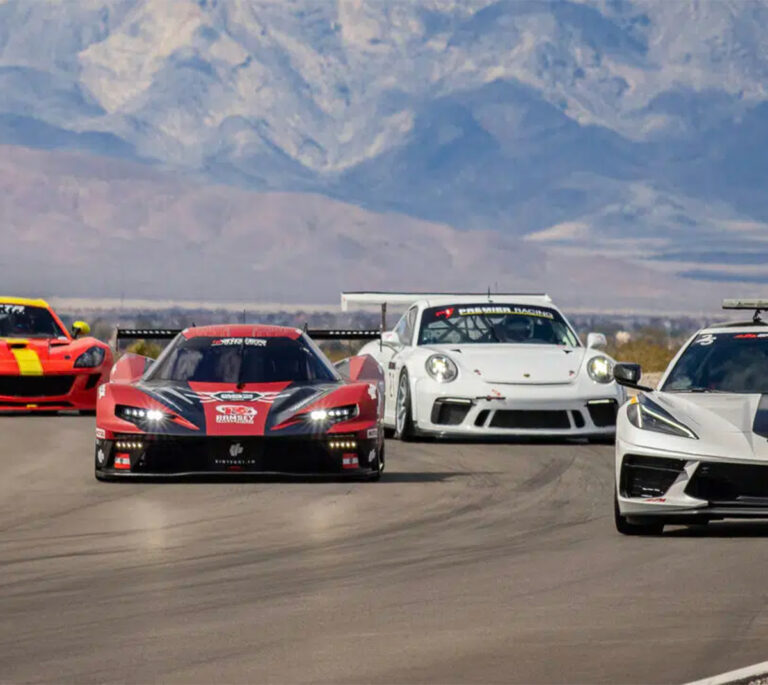 Four sports cars racing on a track with mountains in the background under a clear sky.