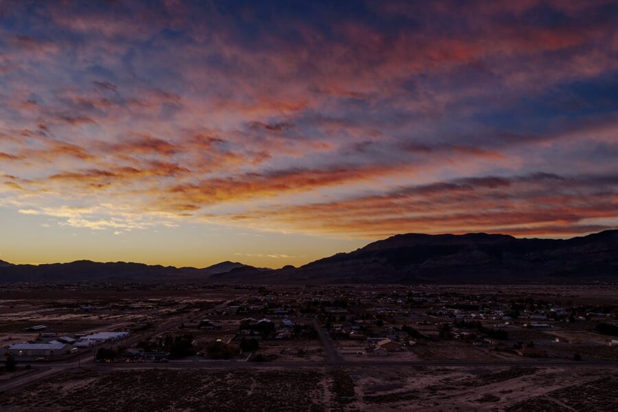 Colorful sunset sky with pink clouds over a small town and distant mountains, landscape in silhouette.