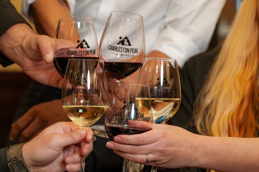 Five people clink Charleston Peak Winery wine glasses filled with red and white wine in a celebratory toast.
