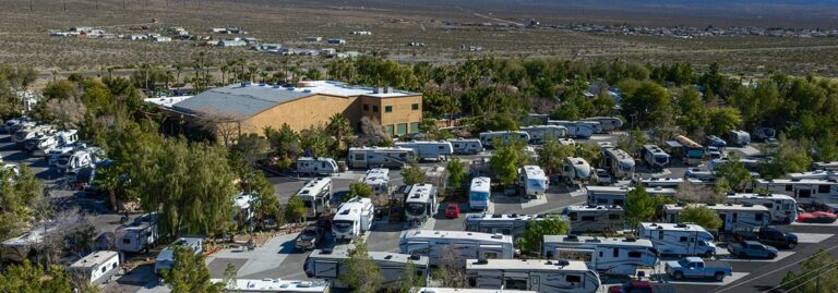 Aerial view of an RV park filled with campers, surrounded by trees and desert landscape in the background.