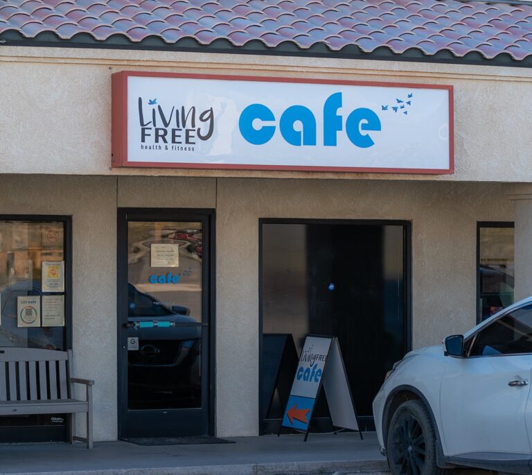 Storefront of Living Free Cafe with a sign, bench, and a car parked in front.